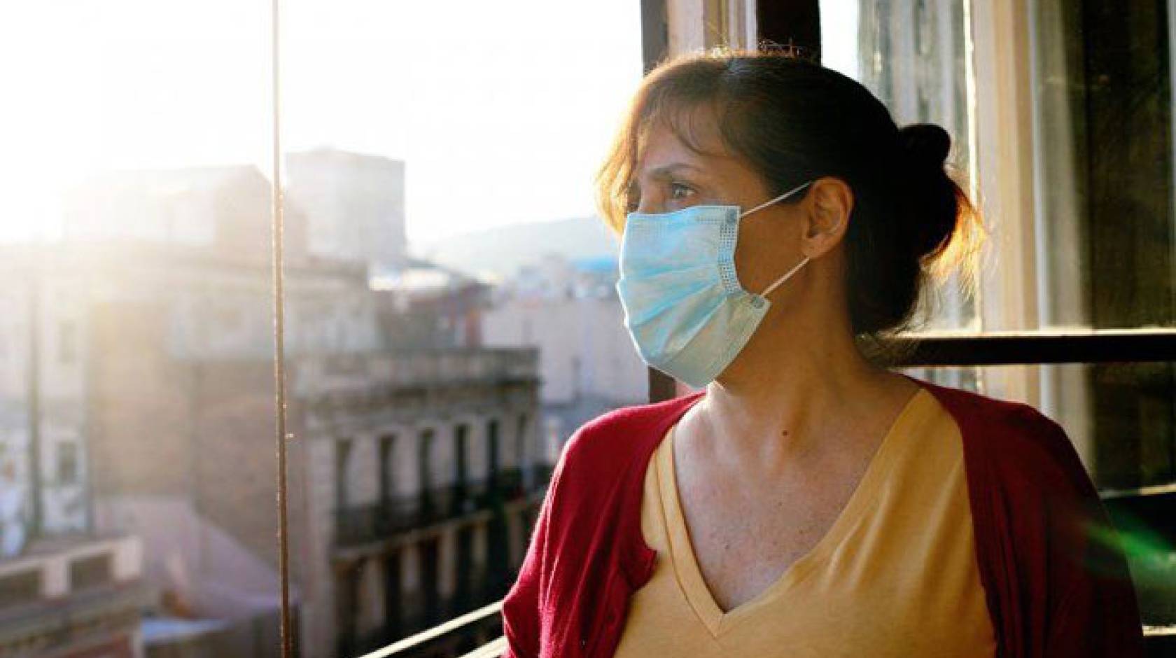 Woman in mask looks out the window