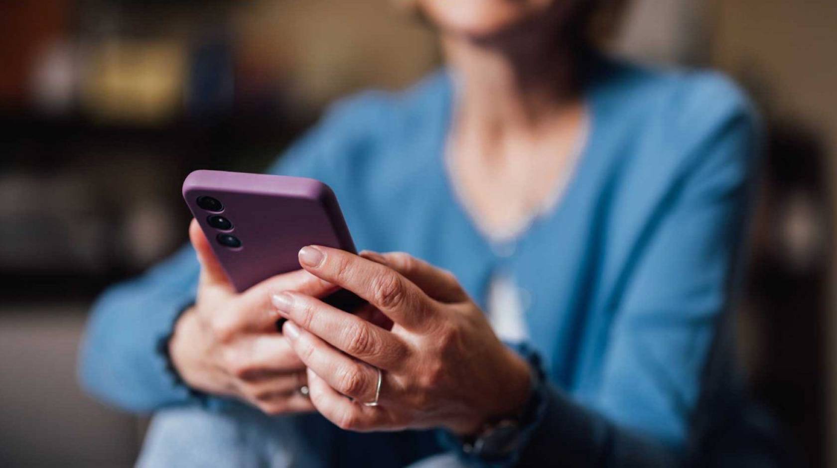 Senior woman uses smartphone; smartphone is central to image, woman's face is cropped out and body blurred