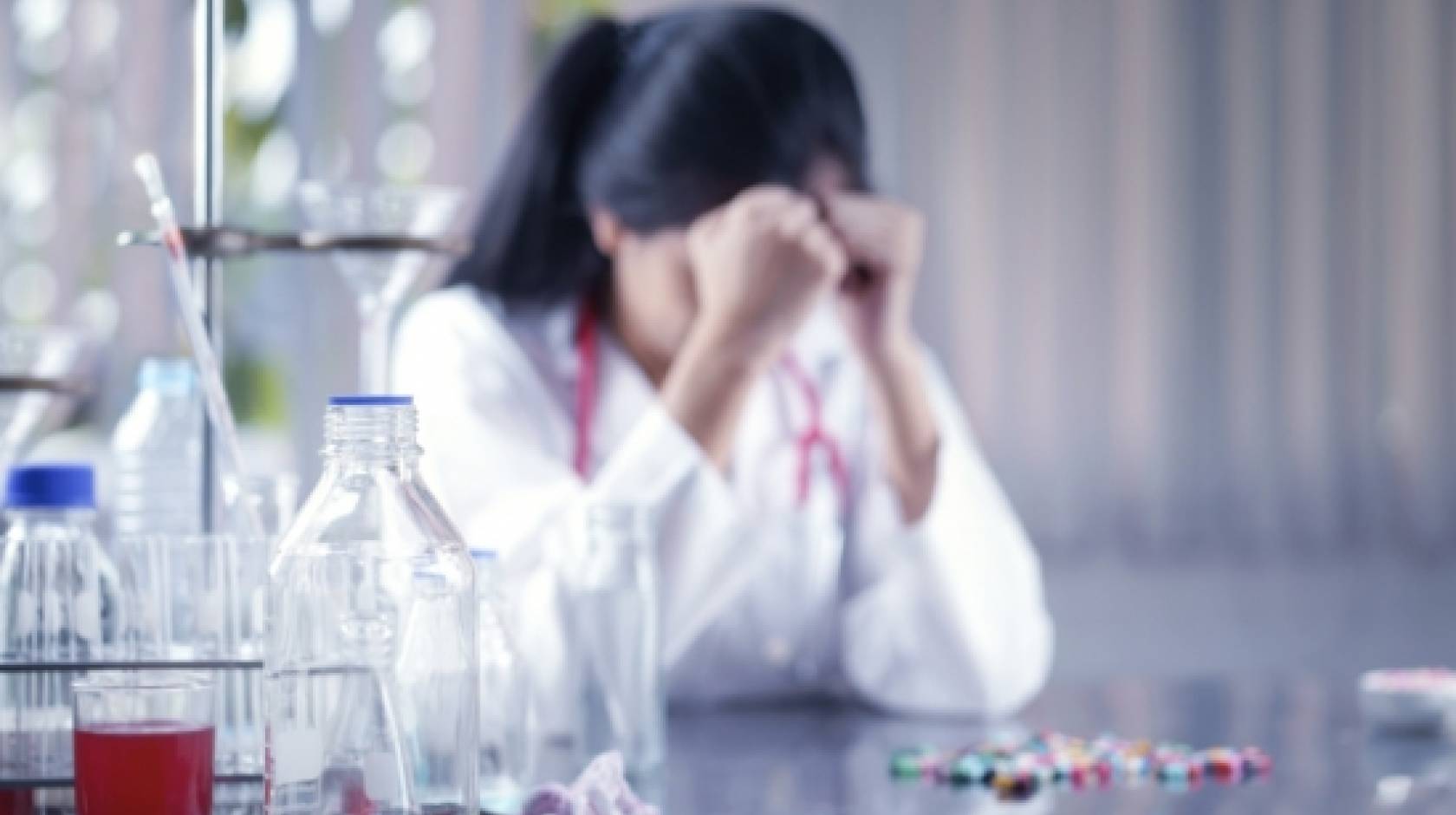 Woman in a lab coat, hangs her head down.