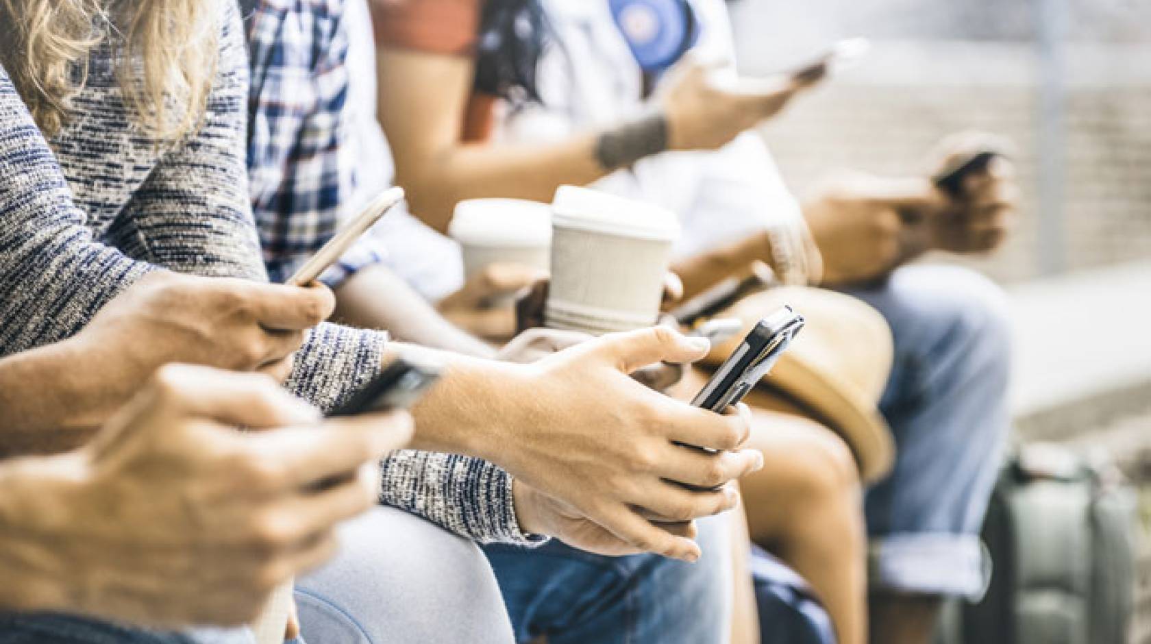 Young adults sitting together on phones no faces visible