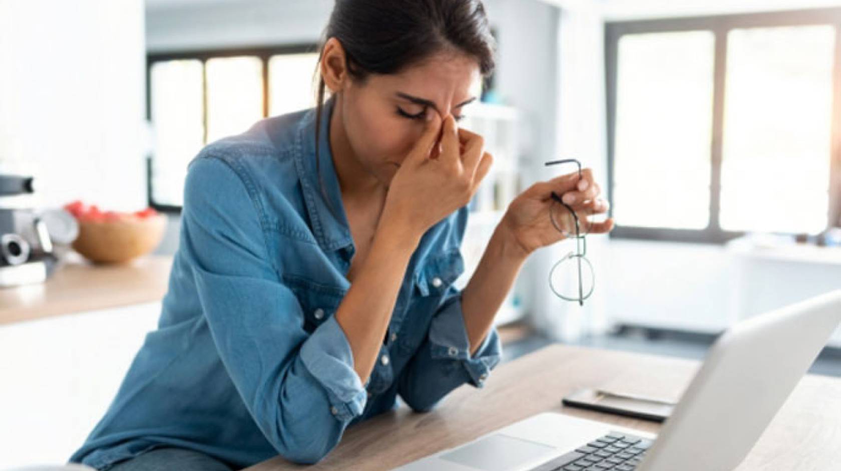 A woman rubs her eyes looking at computer