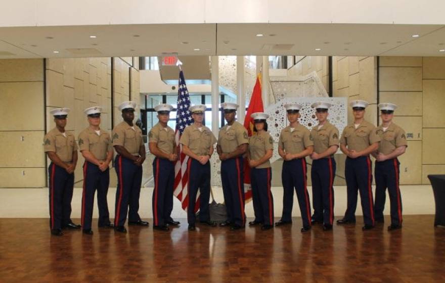 United States Marine Corps veteran and UCI sociology alumnus Andrew Truong ’23 (fourth from right), pictured with fellow service members, posing at ease in their uniforms in front of flags.
