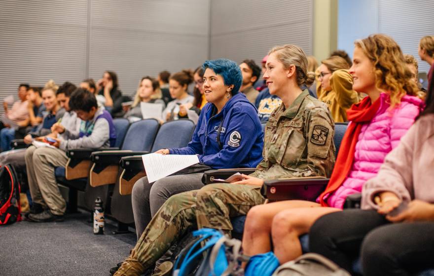 A woman in a U.S. Army uniform sitting in a lecture hall full of students