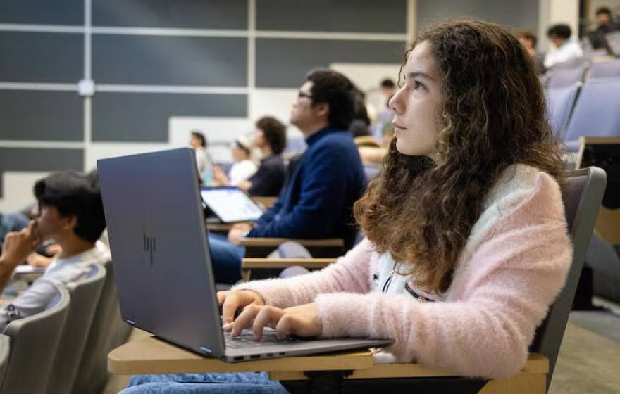 A pre-teen with long hair sits listening in a lecture hall