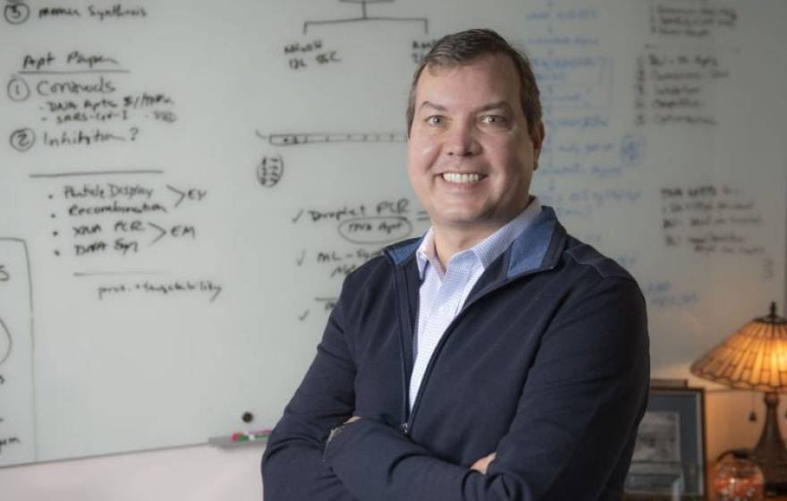 John Chaput, UCI professor of pharmaceutical sciences, stands smiling in front of a white board that is covered with notes.