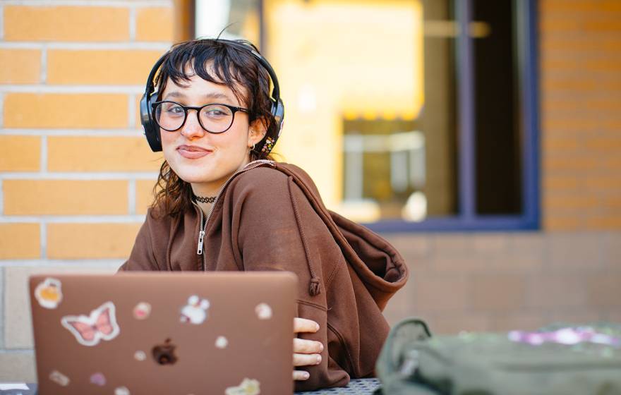 a student sits with an open laptop, smiling