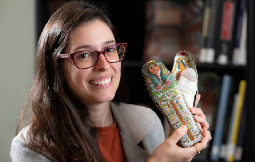 A person smiling and holding a small tin Egyptian coffin