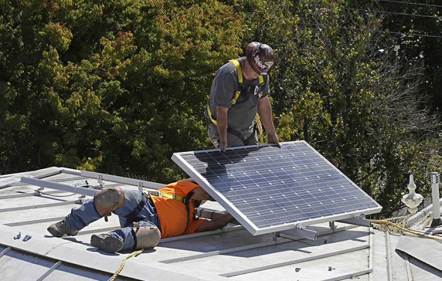 Workers install solar panels on a roof