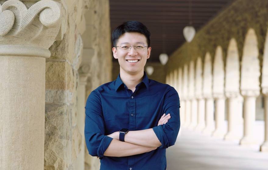 A person standing with crossed arms and smiling in front of a colonnade 