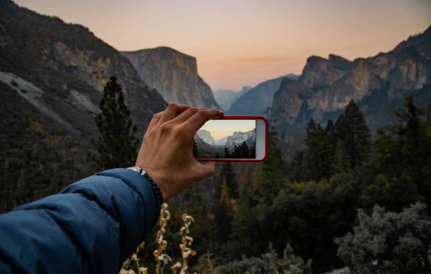 A hand holds a phone up to take a picture at sunset at Tunnel View in Yosemite National Park