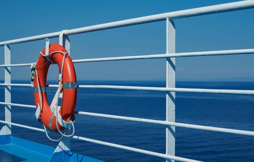 a red lifebuoy hangs on board a ferry cruise ship against the backdrop of a blue sea and a cloudless sky