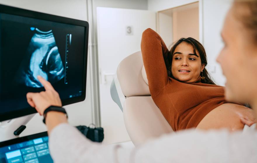 A woman looks happily at an image of her fetus on a screen as a nurse points