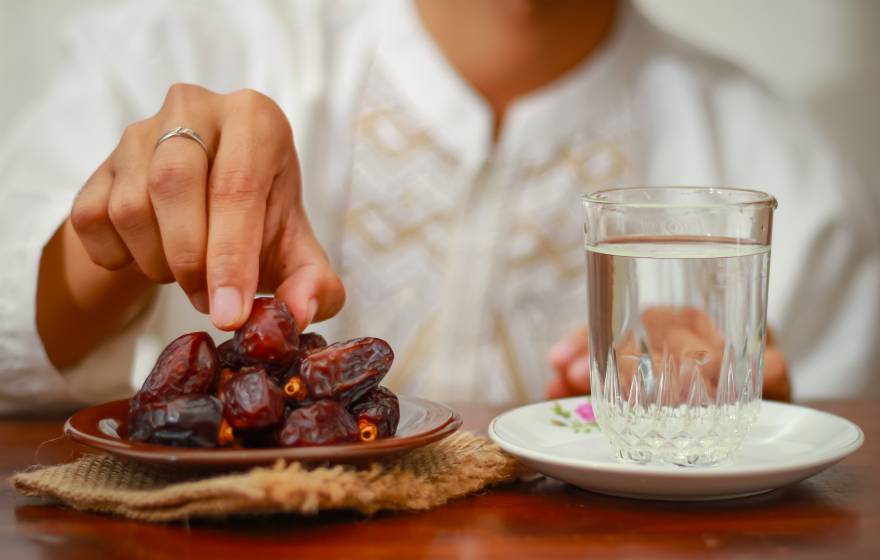 A plate full of dates and a glass of water, with a hand reaching for a date