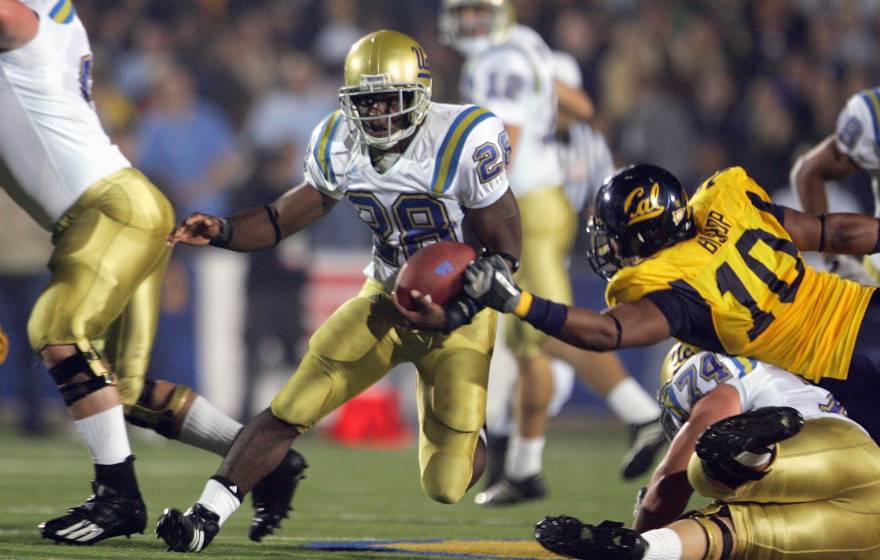 A UCLA football player carries the ball past a diving Cal player while another UCLA player blocks to his right