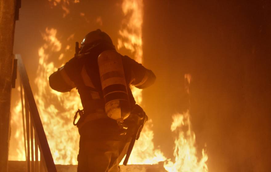 A firefighter with an oxygen cylinder runs up stairs on fire