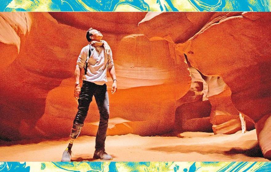 A male hiker with a prosthetic leg below his knee looks up against the backdrop of a red rock canyon wall. The photo is edited and filtered to look grainy, and surrounded by a teal/green textured frame.