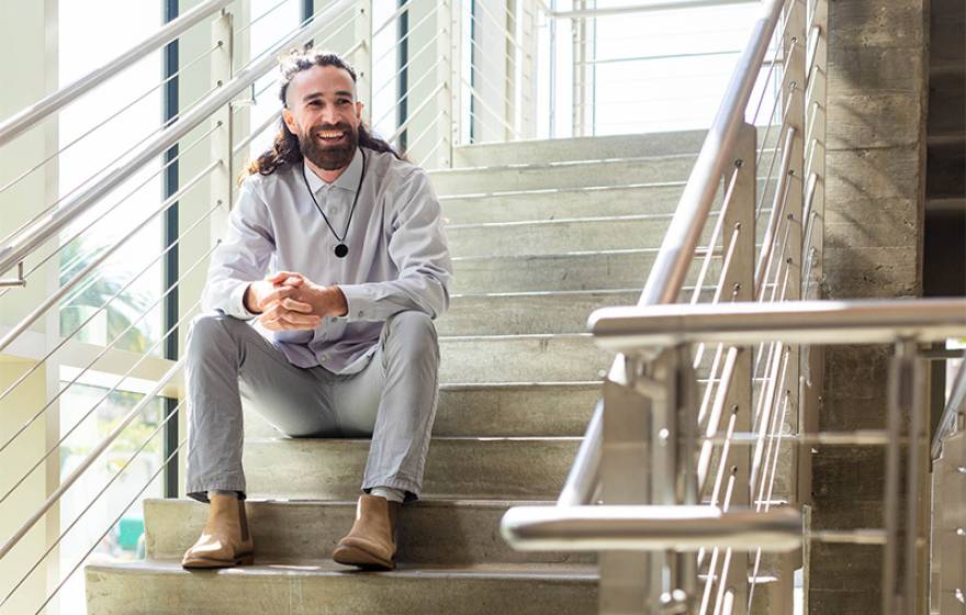 Trevor Auldridge-Reveles sits in a concrete and steel staircase, leaning elbows on legs, smiling