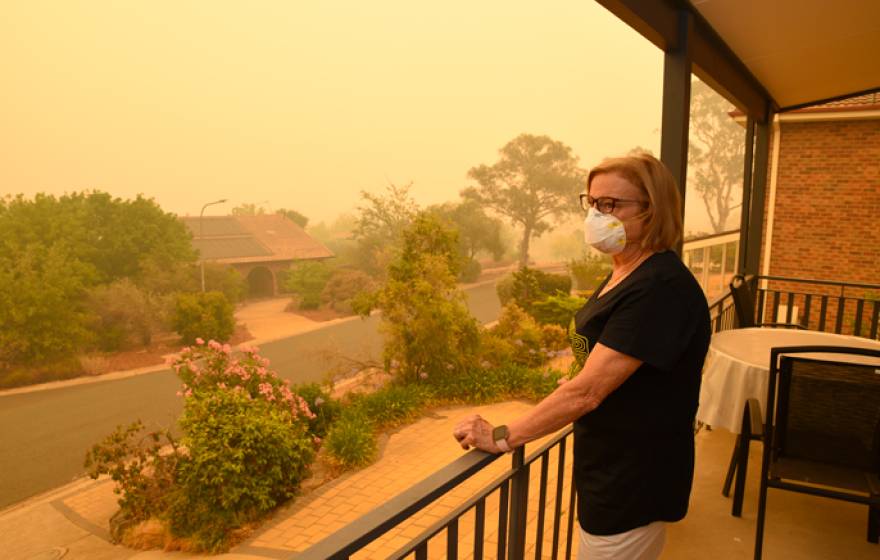 A woman in a mask stares out from her porch at orange air