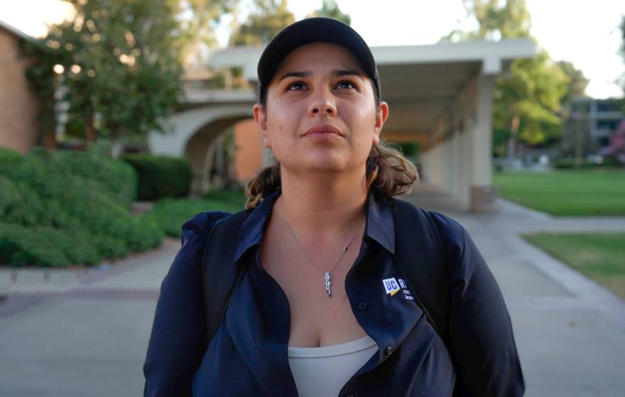 A woman wearing a baseball cap and walking on the UC Riverside campus looks up