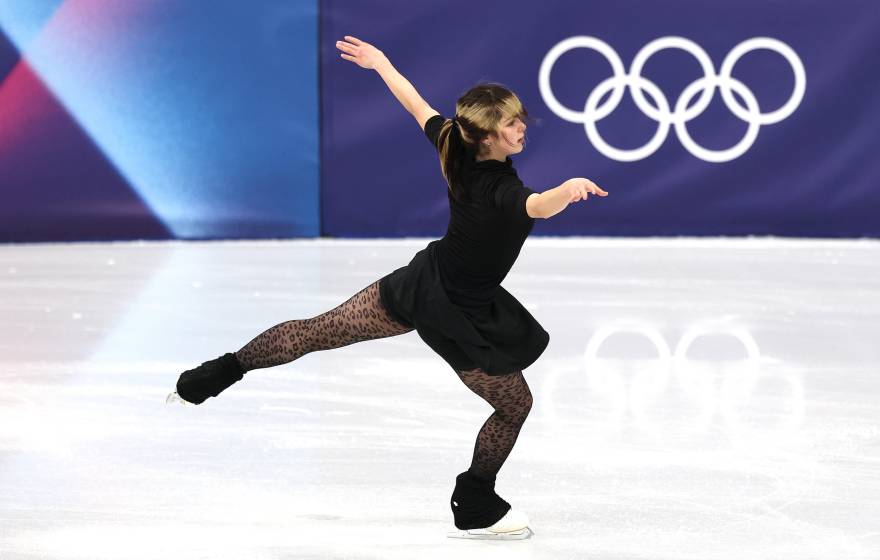 A figure-skating woman woman stretches her arms and back leg while practicing on the ice