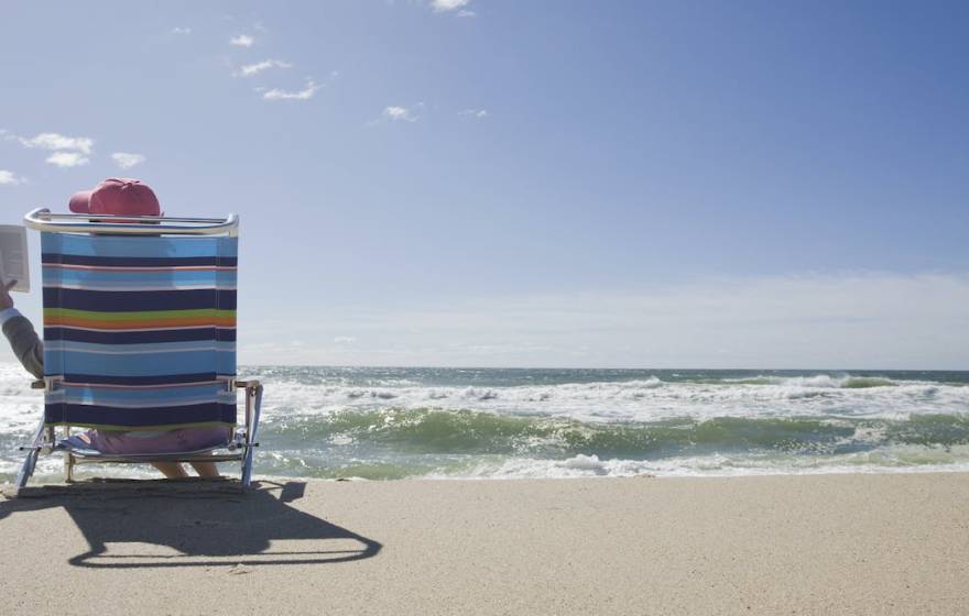 Person reading on the beach, photographed from the back with the ocean in front