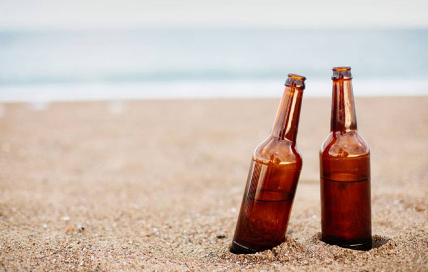 Two half-full beers on a sandy beach