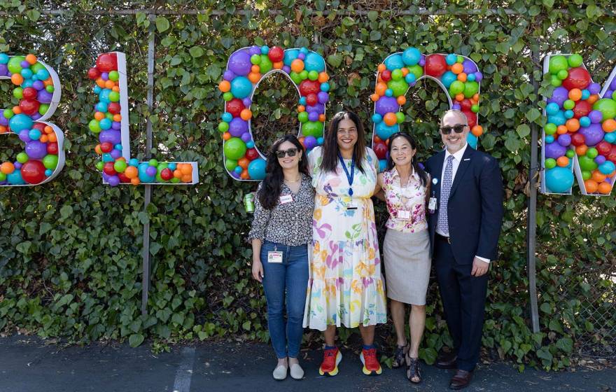 Four people outdoors in front of a sign made of balloons that says 'Bloom'