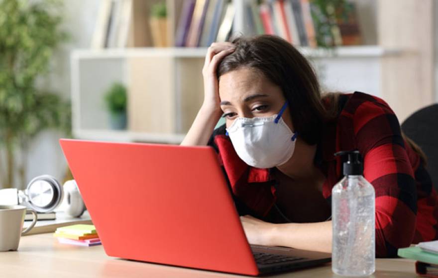 Student in mask looks at computer, bored