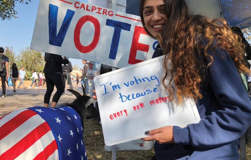 UC Riverside young woman student holds a vote sign next to the vote goat