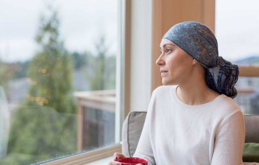 Woman recovering from breast cancer wearing a scarf on her head stares out the window