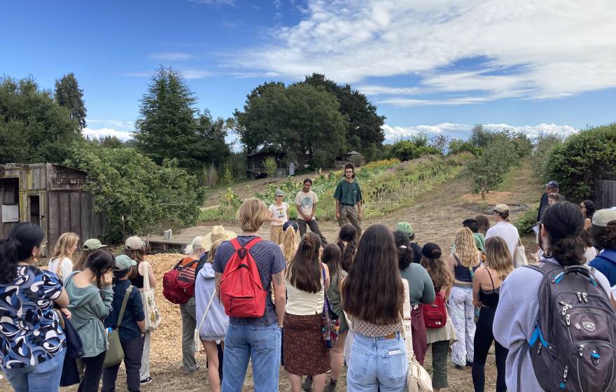 Two people speak to a small crowd of students in a garden