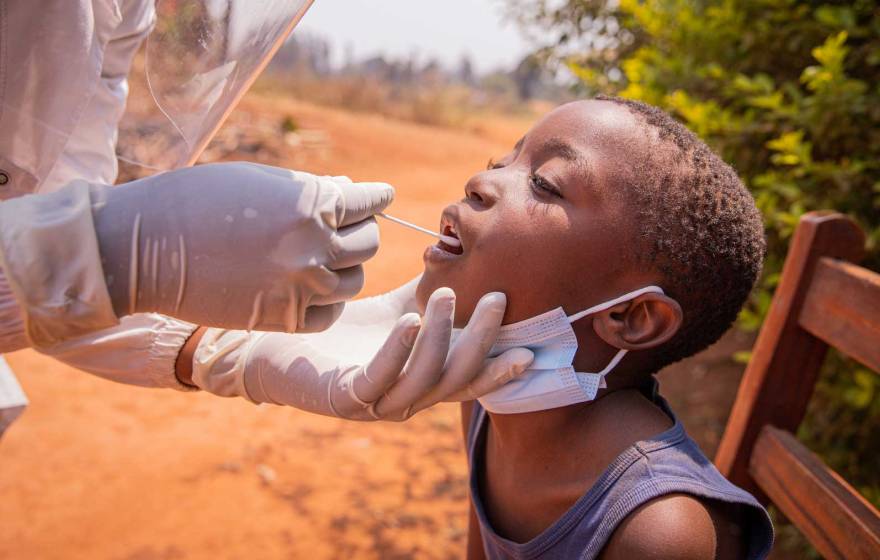 A young African child gets a tongue swab test from a medical professional.