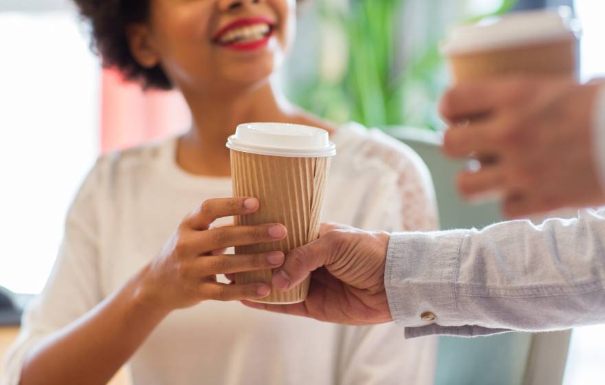 A person hands a smiling Black woman a to go cup of coffee