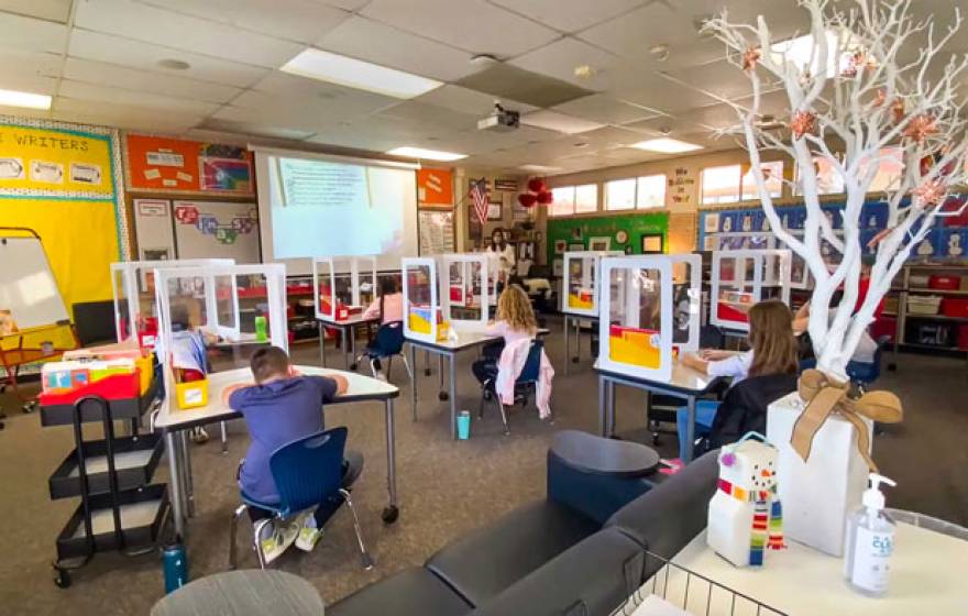 Kids at a school with COVID-19 plastic guards around desks