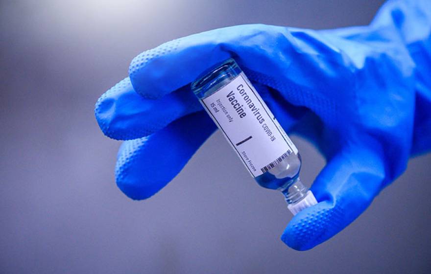 Blue glove holding a COVID-19 vaccine