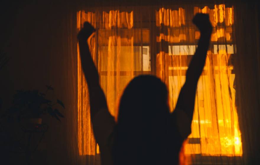 Woman stretching in a room behind curtains that show the dawn