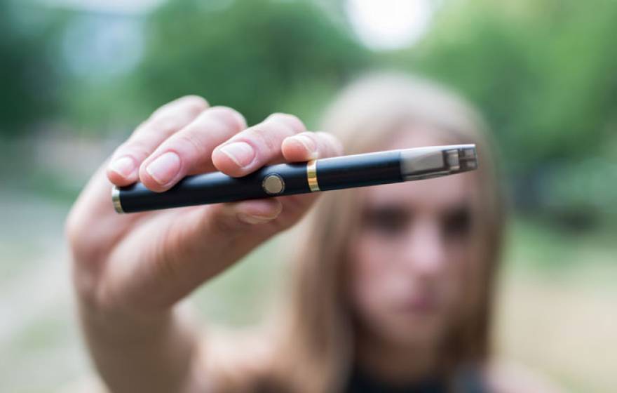 E-cigarette held up by a blurred out teenager