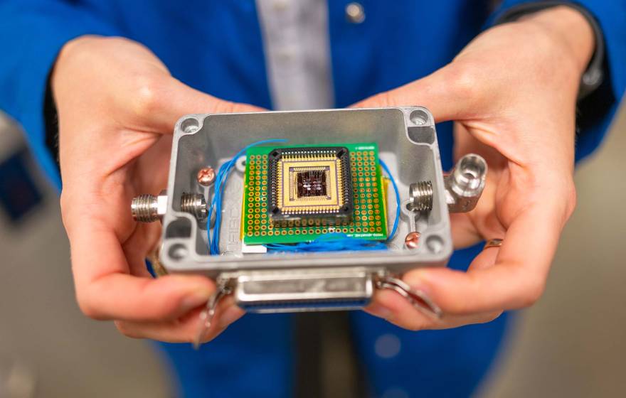 A pair of hands holds a small plastic box that contains a complex electronic chip