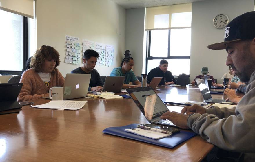 A diverse group of teachers working on laptops together on a wooden table