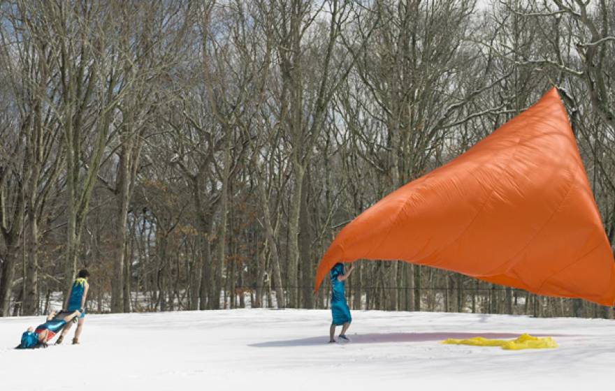 Three people performing with a giant orange sheet outside in the snow