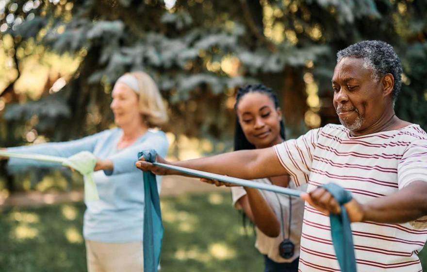 Exercise coach with seniors doing arm exercises with therapy bands