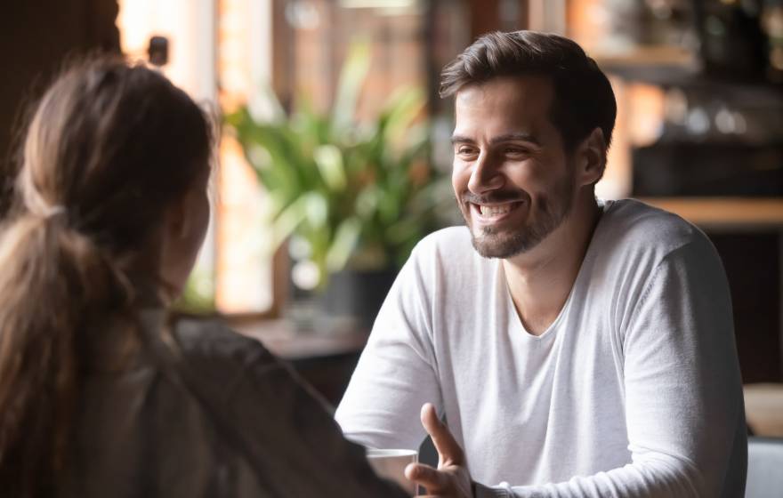 Woman looking at man smiling seated at the same table at a cafe