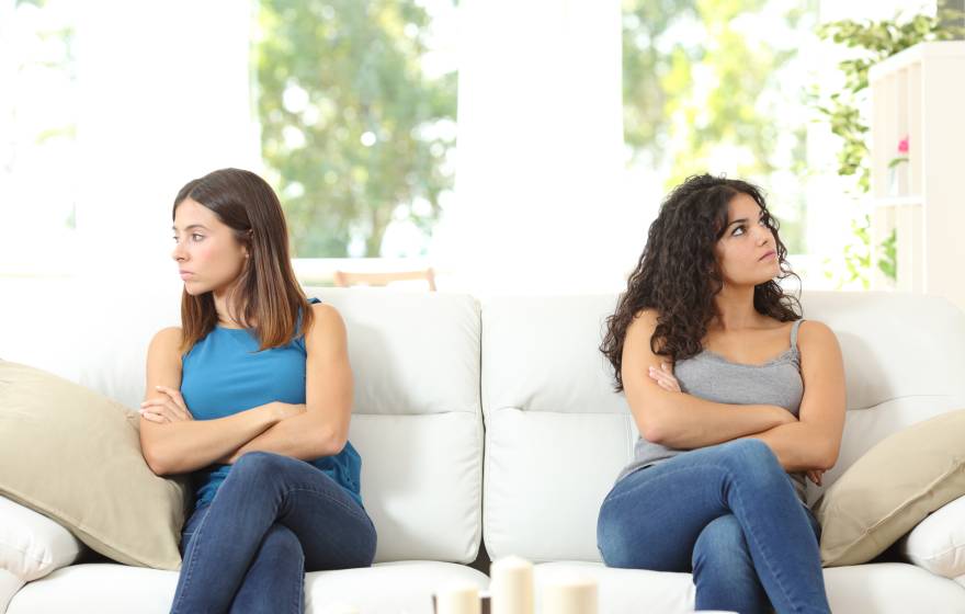 Young women on a couch looking away from each other, arms crossed