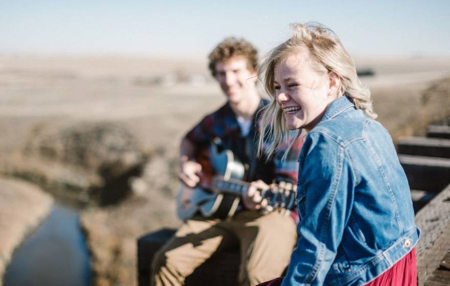 A happy woman smiling as she listens to a man play guitar