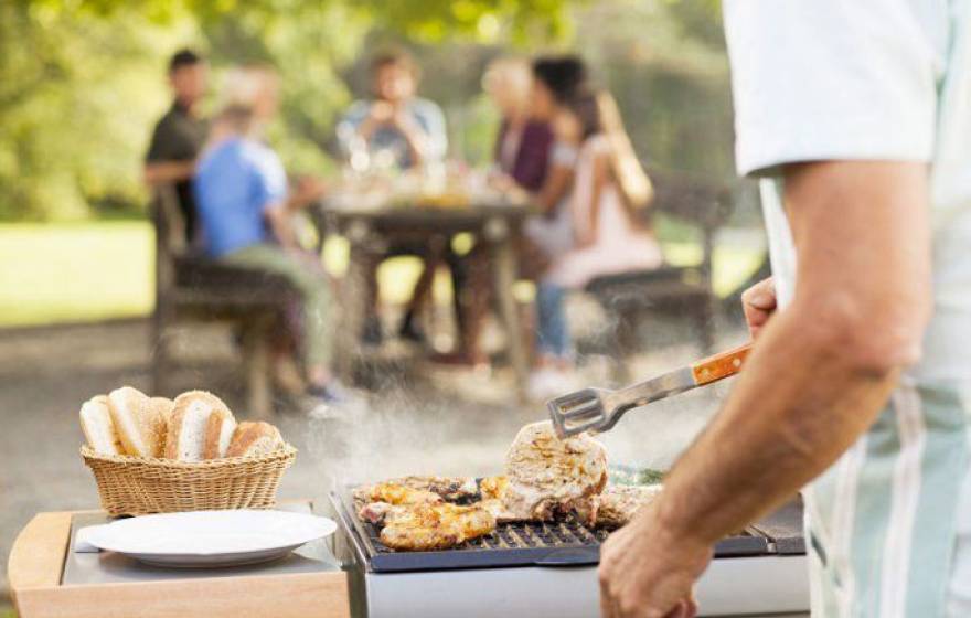 Chicken cooking on a grill with people in the background