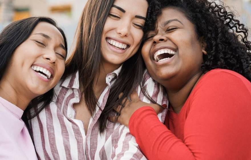 Three women laugh while in a group hug