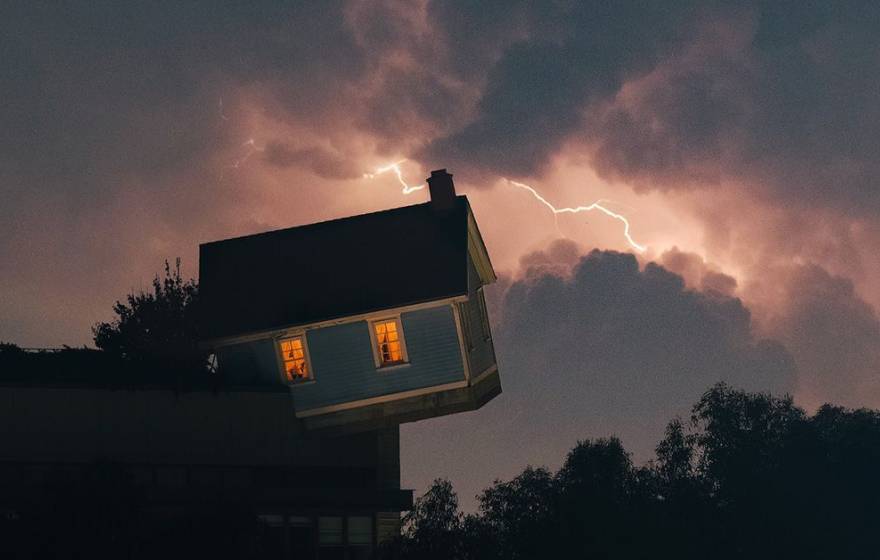The leaning/falling house installation on the UC San Diego campus with a lightning sky backdrop