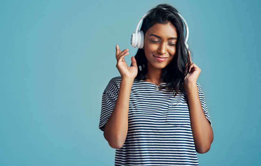 Young South Asian woman listening to headphones smiling and pointing finger