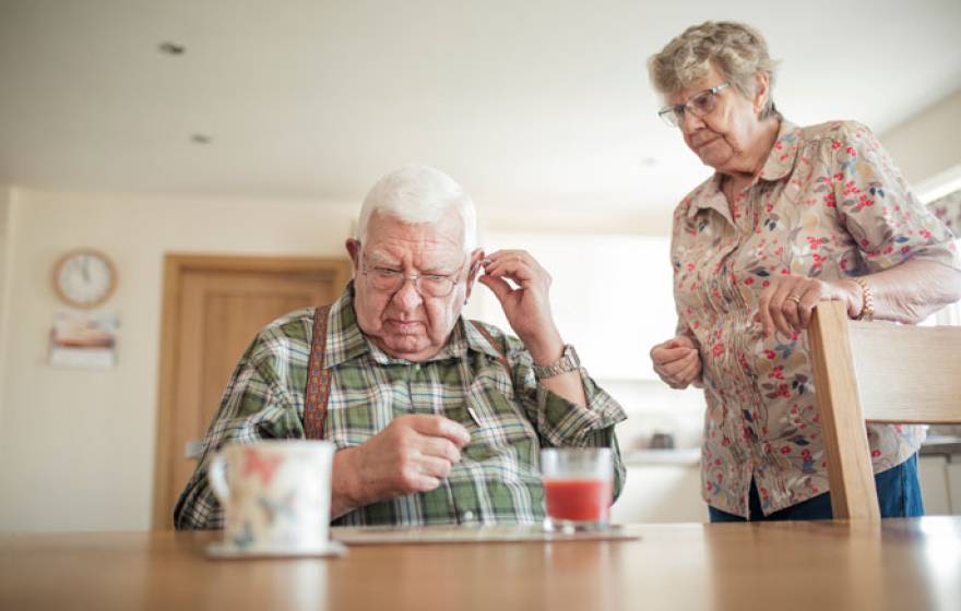 Hearing aid adjusted by senior man with senior woman nearby