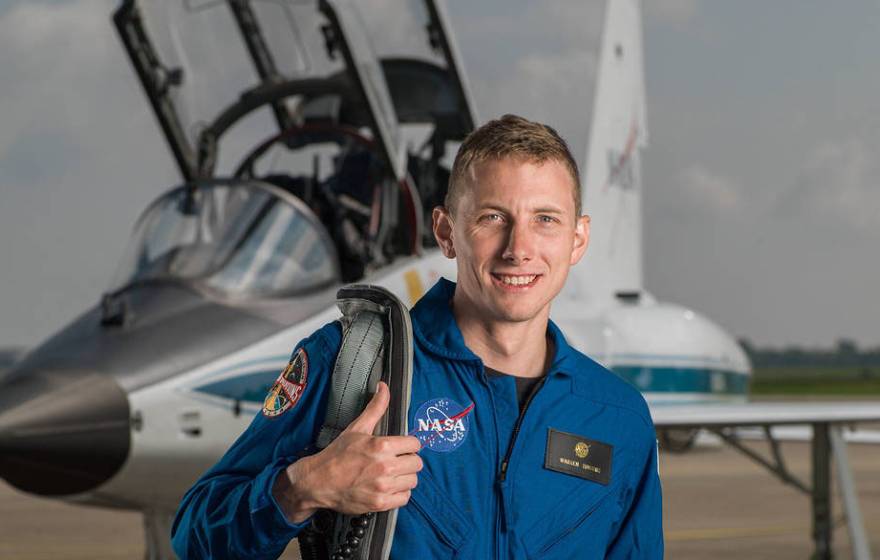 Warren Hoburg in blue spacesuit in front of an aircraft